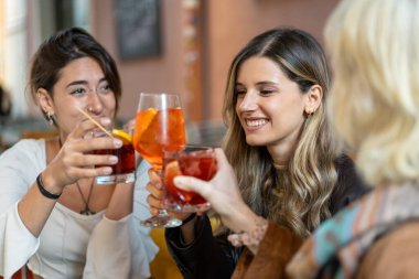 Moda bir barda renkli kokteyllerle kadeh kaldıran ve arkadaşlarıyla eğlenen üç zarif genç kadının yakın çekimi..