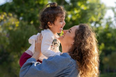 Sevgi dolu bir anne, annelik ve aile bağının neşesini kutlamak için, gülen çocuğunu altın saat boyunca parkta kaldırır..