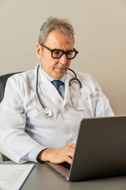 Başhekim muayenehanesinde dizüstü bilgisayar kullanıyor, işine ve internet danışmanlığına odaklanmış..