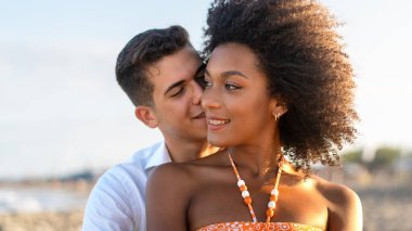 Gülümseyen ırklar arası bir çift gün batımında sahilde romantik bir anın tadını çıkarıyor..