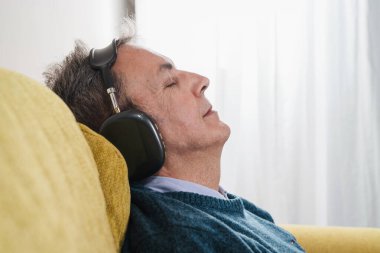 Ses geçirmez kulaklık takan, gözleri kanepeye kapalı dinlenen son sınıf öğrencisinin yakın çekimi. Rahatlama, farkındalık ve dijital refah kavramı.