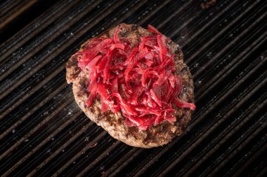 Izgara ızgara ızgara ızgaranın üstünde kırmızı soğanlı sulu ızgara burger köftesi. Duman ve ızgara izleri taze pişmiş eti vurguluyor..