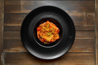 Kiraz domatesli gurme makarna, çıtır çıtır sos ve ahşap bir masada, siyah bir tabakta zarif bir şekilde servis edilen lezzetli bir sos..