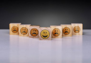 Yazılı gülen yüzlü ahşap bloklar seti. Tek bir sarı gülen yüz hüzünlü ifadeler arasında yer alıyor. Pozitiflik, liderlik, eşsizlik ve bireysellik kavramı.