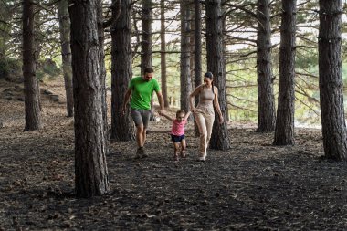 Mutlu ebeveynler ormanda kızlarıyla el ele yürür, doğanın ve birlikteliğin tadını çıkarırlar.