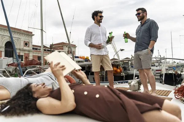 Tekne güvertesinde bir grup arkadaş marinada dinlendirici bir yaz gününde içki içip kitap okuyorlar.