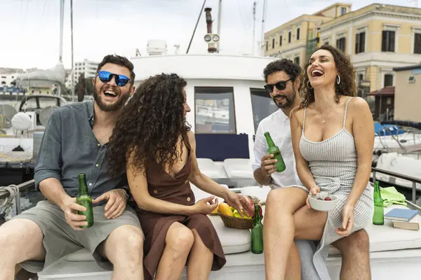 Bir grup mutlu yetişkin arkadaş bir teknede bira içerken rahatlıyor ve gülüyorlar, marinada yaz tatilinin tadını çıkarıyorlar.
