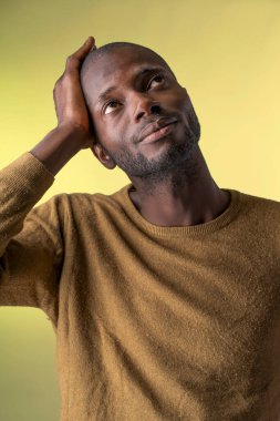 Kafasına dokunan düşünceli bir adamın yakın plan portresi, sarı arka planda stüdyoda çekildi.