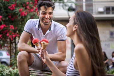 Mutlu genç çift dışarıda oturmuş yazın birlikte çilekli dondurmanın tadını çıkarıyor, gülümsüyor ve gülüyorlar..