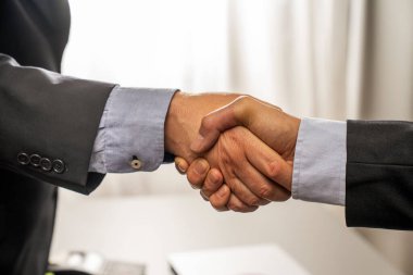 İki profesyonelin ofis ortamında el sıkışması başarılı bir pazarlığın sonunda ortaklığı, anlaşmayı ve karşılıklı güveni sembolize eder..