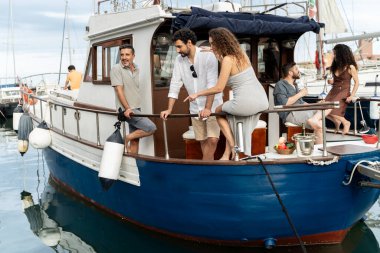 Bir grup yetişkin, Akdeniz marinasında demirli küçük bir yatta takılıp sohbet ediyor ve şarap içiyor. Yaz tatili, tekne kiralama ve arkadaşlarla boş bir yaşam tarzı..