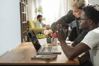 Parlak bir ofis ortamında, siyahi bir adam ve bir bayan meslektaşı bir dizüstü bilgisayarın üzerine eğilip, üretken bir çalışma sırasında gülümsemeyle işbirliği yapıyorlar..