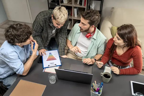 Renkli bir huni grafiğini inceleyen ve sıradan bir ofiste dizüstü bilgisayarın etrafında dijital pazarlama stratejisi planlayan çok kültürlü genç iş arkadaşlarının en alt basamağı..