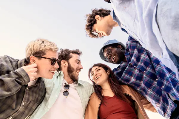 Çeşitli genç yetişkinler aşağıdan bir daire şeklinde gülümsüyor. Arkadaşlık, birlik ve toplum bağları kavramı.