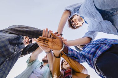 Çeşitli genç arkadaşlar aşağıdan el ele tutuşuyorlar. Birlik, işbirliği, gençlik takım çalışması ve arkadaşlık kavramı.