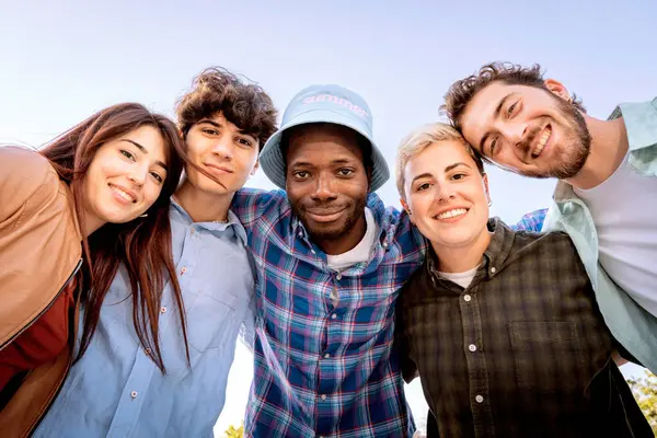 Bir grup neşeli, çok ırklı genç arkadaş açık havada birlikte gülümsüyor, birlik ve arkadaşlık kavramı.