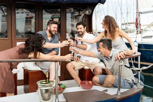 Altı yetişkin arkadaş motorlu teknenin güvertesinde kutlama yapıyor, köpüklü şarapla kadeh kaldırıyor ve marinada bir yaz gezisi sırasında gülüyorlar. Lüks seyahat, arkadaşlık, denizde boş zaman geçirme kavramı.