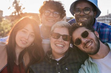 Çeşitli genç arkadaşlar gün batımında birlikte dışarıda vakit geçiriyorlar, gülümsüyorlar ve gerçek dostluğu ve mutluluğu kucaklıyorlar.