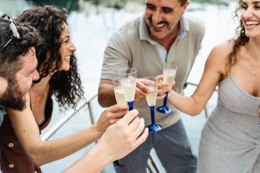 Mutlu çok kültürlü arkadaşlar yatın güvertesinde şampanya bardaklarını tokuşturup yaz tatilini denizde kutluyorlar..