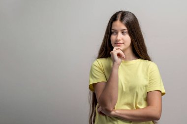 Young brunette in yellow shirt with hand on chin, looking aside thoughtfully. Ideal for concepts of strategy, introspection, or future ideas, with ample room for text on a plain studio backdrop.