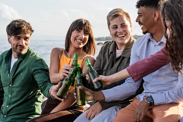 Bir plaj partisi sırasında gün batımında bira şişeleriyle gülümseyen ve tezahürat yapan çok kültürlü bir arkadaş grubu..