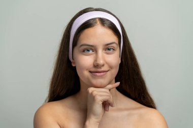 Açık tenli ve minimum makyajlı güzel genç bir kadın kameraya hafifçe gülümsüyor. Cilt bakımı, sağlık ve kendine güvenen bir ifadeyle doğal güzellik portresi..