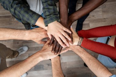 Diverse group of people joining hands in circle, symbol of unity, trust, teamwork and friendship.