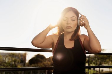 Huzurlu bir kadın gözleri kapalı dinlendirici bir müzik dinler ya da kulaklıklarıyla meditasyon yapar, dışarıda huzurlu bir anın tadını çıkarır.