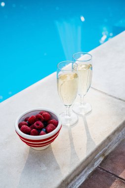 Yazın yüzme havuzunun yanında iki bardak köpüklü şampanya ve taze böğürtlen. Sosyal medya hikayeleri için mükemmel bir dikey fotoğraf lüks veya kutlama hakkında