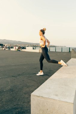 Atletik bir kadın, kalabalık bir şehir parkında arka planda diğer insanlarla birlikte hareket egzersizi yapıyor. Açık hava sporu kavramı..
