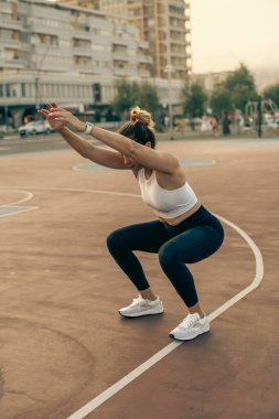Atletik bir kadın vücut ağırlığı antrenmanı sırasında şehir kortunda düzgün bir şekilde çömelir.