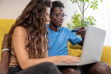 Çevrimiçi alışveriş için kredi kartı ve dizüstü bilgisayar kullanan veya evden birlikte rezervasyon yapan farklı bir çift..