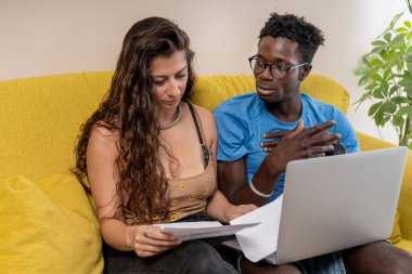 Genç bir çift kanepede oturur ve ev işlerinde işbirliği yapar. Evrakları dizüstü bilgisayarla incelerler..