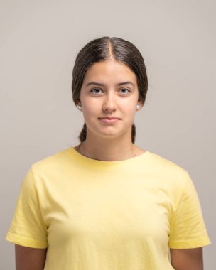 Siyah saçlı ve kameraya bakan tarafsız bir yüz ifadesiyle güzel bir genç kadının vesikalık fotoğrafı..