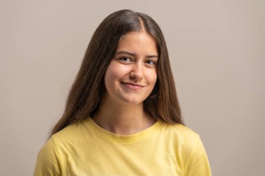 Nazik, otantik bir gülüşü olan güzel bir genç kızın yakın plan fotoğrafı. Stüdyo geçmişine karşı gerçek bir insanın doğal ve dostane bir portresi..