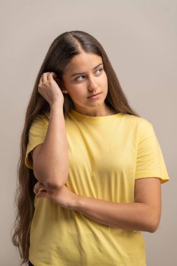 Düşünceli ve düşünceli genç bir kadın uzun saçlarına hafifçe dokunurken düşüncelere dalmış ya da hayal kuruyor..