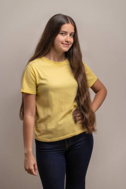 Uzun saçlı, kendinden emin ve arkadaş canlısı genç bir kadın eli kalçasında kameraya gülümsüyor. Tarafsız bir geçmişi olan bir stüdyoda basit, doğal bir portre..