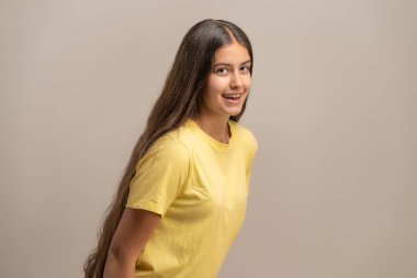 Uzun saçlı, güzel ve neşeli genç bir kadın arkasını dönüp kameraya mutlu bir şekilde gülümsüyor. Tarafsız bir stüdyonun arka planına doğru..