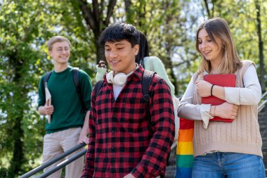 Gökkuşağı gururlu aksesuarları olan, güneşli bir kampüste birlikte yürüyüp gülümseyen bir grup öğrenci arkadaş. Gençlik, kapsama, arkadaşlık ve modern öğrenim hayatı kavramları.
