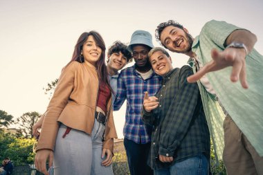 Farklı etnik çeşitlilikteki bir grup arkadaşın birlikte gülüp eğlendiği, güneşli bir günde dışarıda eğlendiği otantik ve samimi bir an..