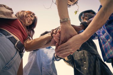 Çeşitli gençlerden oluşan bir grubun düşük açılı yakın çekimi ellerini merkezde birleştirerek takım çalışmasını, birliği, desteği, güveni ve başarılı işbirliğini sembolize ediyor..