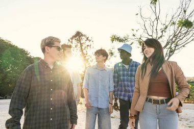 Bir grup neşeli genç arkadaş yan yana yürüyor ve güzel, sıcak bir altın saat boyunca parkta rahatça sohbet ediyorlar..