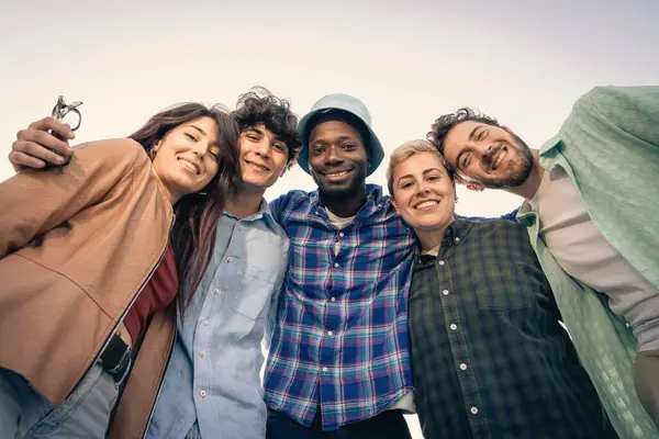 Neşeli ve çeşitli yetişkin arkadaşlar kollarını birbirlerine dolayıp, kameraya bakıyorlar ve güzel, sıcak bir altın saat günbatımında parkta birlikte gülümsüyorlar..