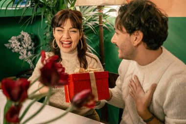 Genç bir adam samimi ve otantik bir Noel partisinde arkadaşlarıyla samimi, şenlikli bir restoranda sohbet ederken sıcak bir şekilde gülümsüyor..