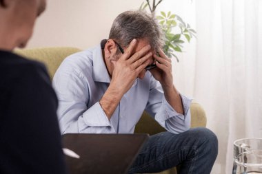 Bir terapistle terapi seansı sırasında stres, depresyon ya da keder belirtileri gösteren aşırı gelişmiş bir adam başını elinde tutuyor..