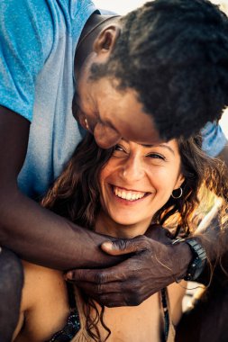 Mutlu, çok kültürlü bir çift açık havada sevgi dolu bir anı paylaşıyor. Gözlüklü, aşk, çeşitlilik, arkadaşlık, yakınlık, ilişki, neşe ve otantik yaşam tarzı ile kucaklanan gülümseyen kadın.