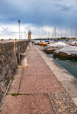 Desenzano, Garda Gölü, İtalya - 25 Mayıs 2024 Limandaki renkli balıkçı tekneleri ve deniz feneri. 