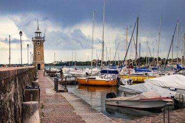 Desenzano, Garda Gölü, İtalya - 25 Mayıs 2024 Limandaki renkli balıkçı tekneleri ve deniz feneri. Yüksek kalite 3d illüstrasyon
