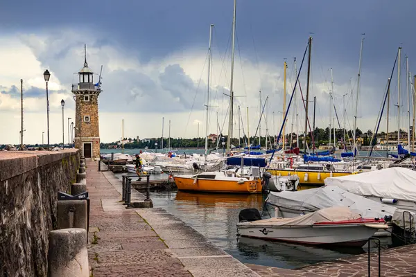 Desenzano, Garda Gölü, İtalya - 25 Mayıs 2024 Limandaki renkli balıkçı tekneleri ve deniz feneri. Yüksek kalite 3d illüstrasyon