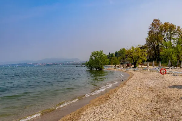 Sezon başında boş güneşlikler Pacengo, Garda Gölü, İtalya 'daki beyaz çakıl taşlı plajlarda. 
